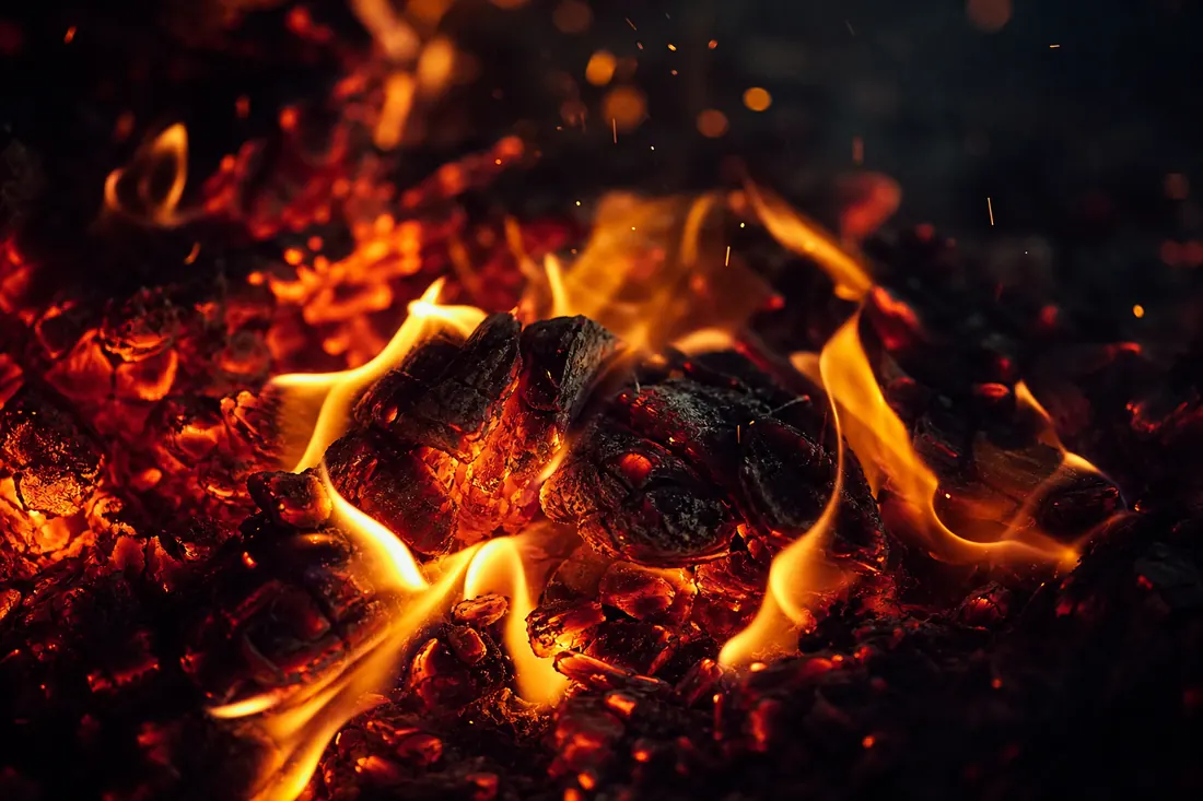Slow-burning embers and low flames in close-up against black
